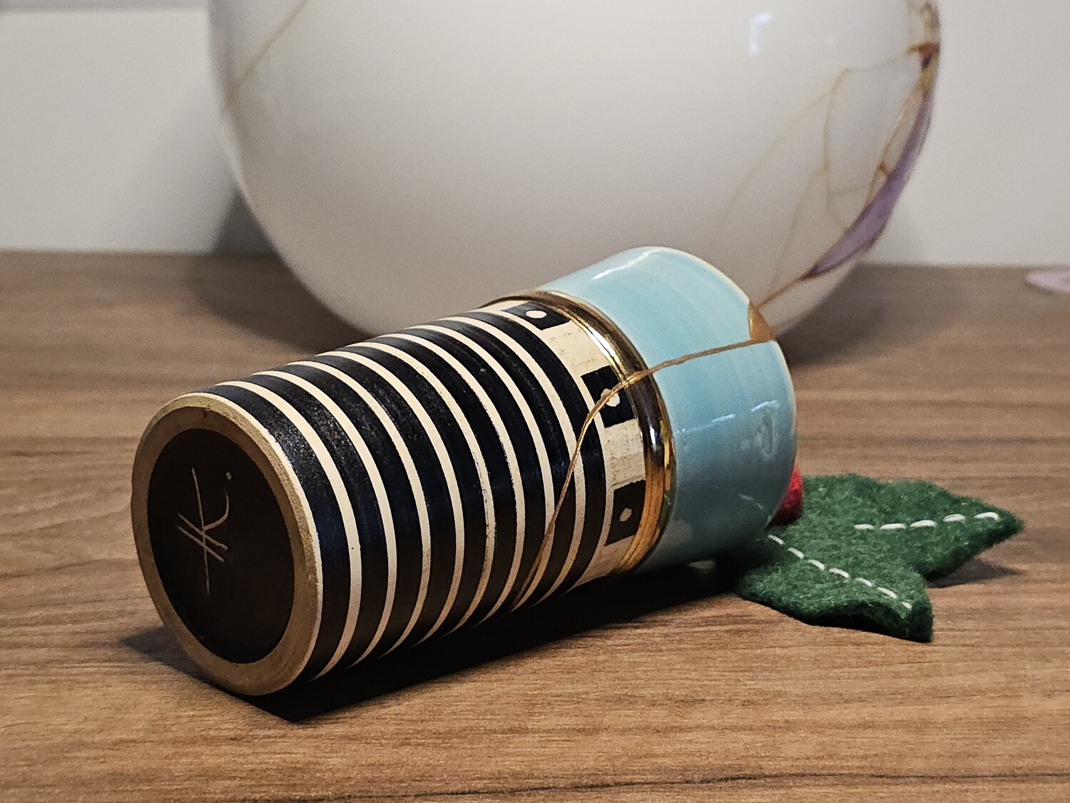 The repaired mug lying on its side. Below is a decorative green leaf and behind a glass globe lampshade.