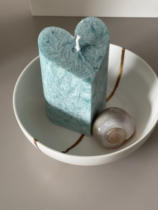 The repaired bowl presented with a large, white-blue marble like patterned candle and an artistic snail shell.